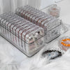Clear jewelry organizer boxes filled with various beads and stones resting on a white fluffy surface.