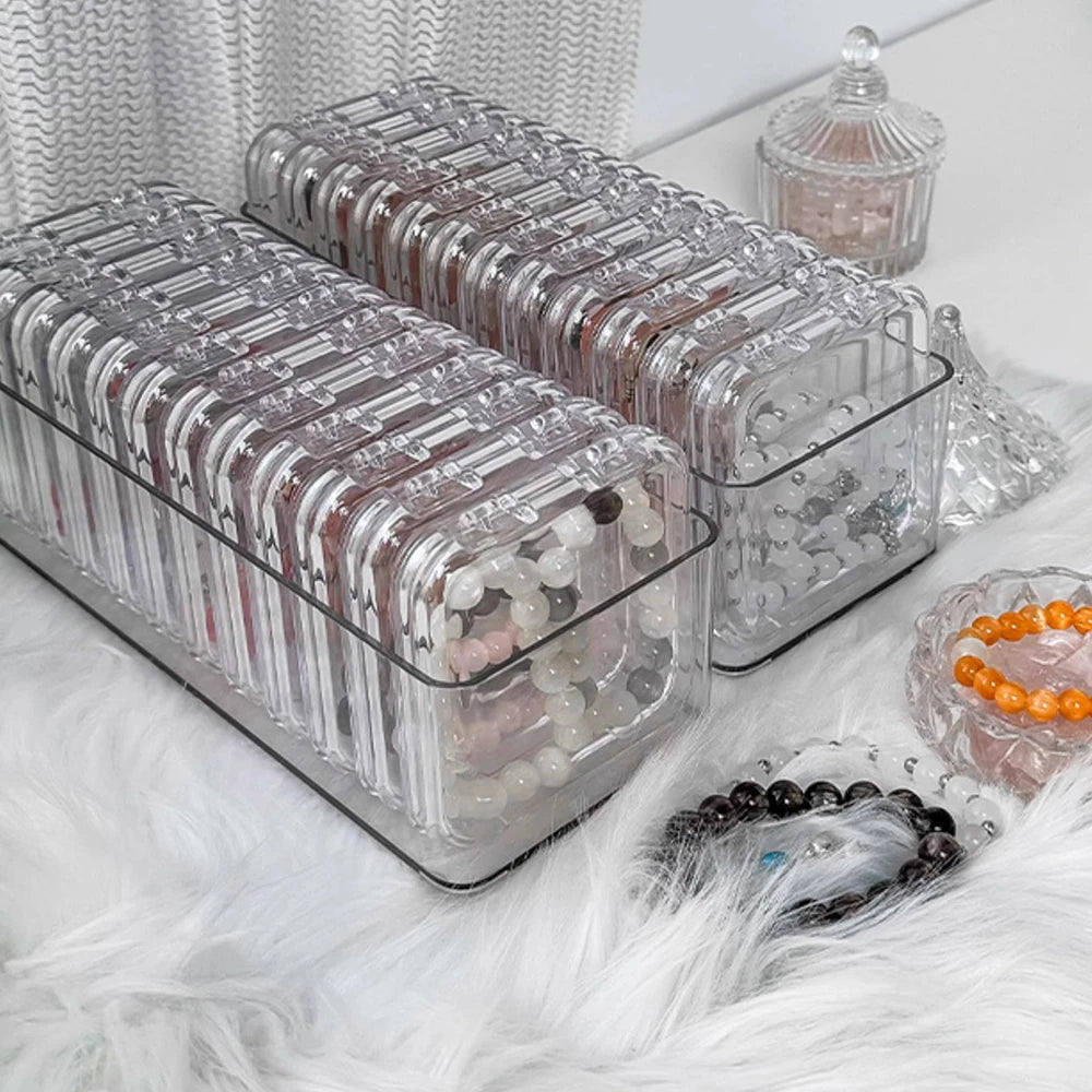 Clear jewelry organizer boxes filled with various beads and stones resting on a white fluffy surface.