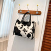 A black and white faux fur leopard print tote bag is hanging on a white wall.