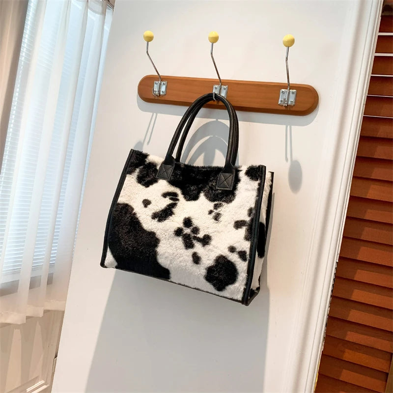 A black and white faux fur leopard print tote bag is hanging on a white wall.