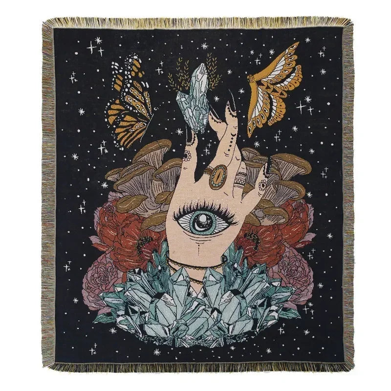 A dark woven blanket featuring a stylized hand with an eye surrounded by floral and feather motifs against a starry backgroun