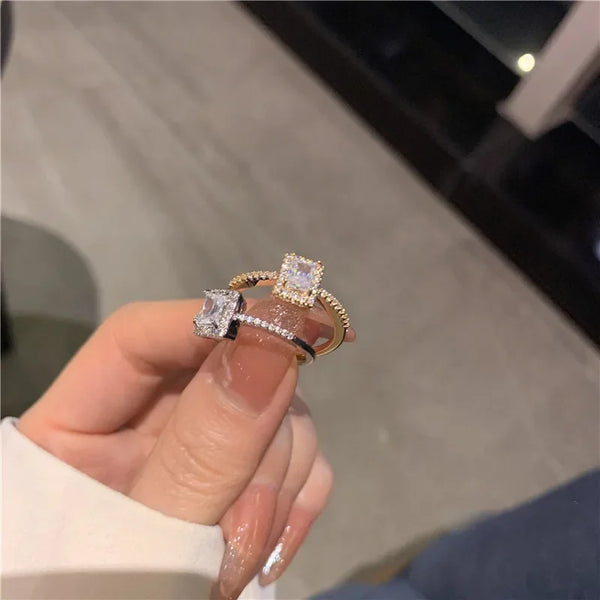 Una mano sostiene un anillo geométrico clásico de zirconia con banda ajustable abierta, mostrando la piedra brillante y su en