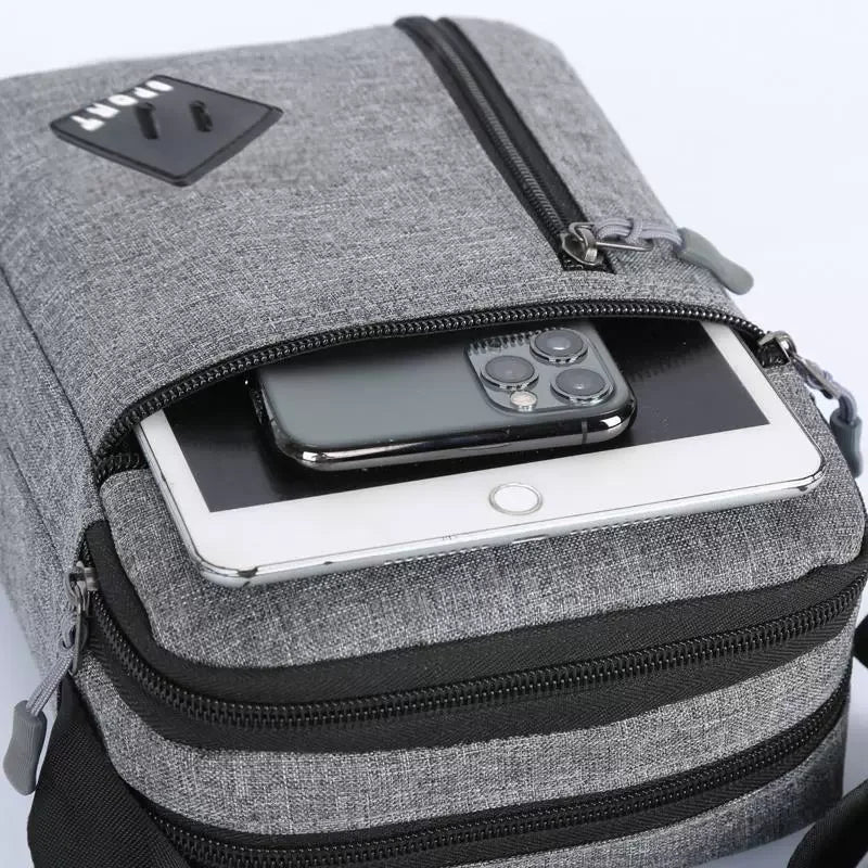A gray lightweight crossbody sling bag with a zippered pocket holding a smartphone.