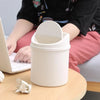 A white compact covered desktop trash bin with a flip lid sitting on a wooden table.