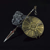 A metal sword keychain and collectible ornament featuring a blade and a circular, textured gold medallion resting on a dark r