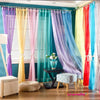 A collection of sheer voile curtains in various pastel colors like purple, yellow, pink, and blue hanging in a window.