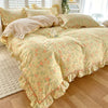 A floral ruffle cotton duvet cover set in pale yellow with pink and green accents on a bed.
