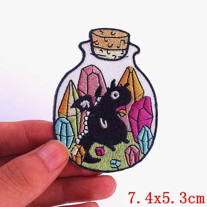 Embroidery patch featuring a black cartoon cat surrounded by colorful gemstone shapes on a white fabric background.