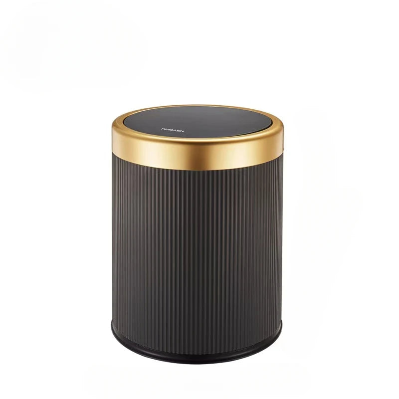 A cylindrical trash can with a black textured body and a gold rim and lid.