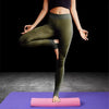 A person wearing olive green athletic leggings is standing on a pink foam roller on a purple mat.