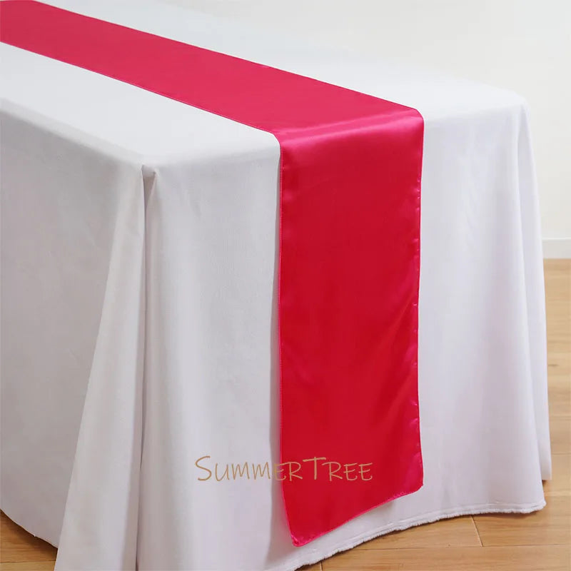 Elegant satin table runner in bright pink draped across a white tablecloth.