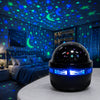 A black spherical projector emitting blue light and stars onto a bedroom wall decorated with a starry sky pattern.
