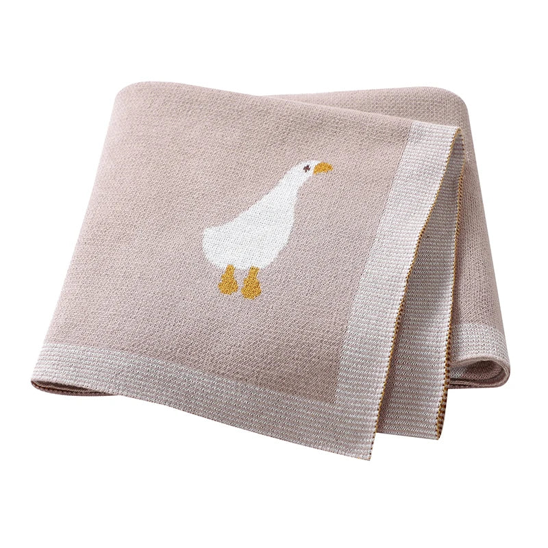 A beige soft cotton baby swaddle blanket featuring a white cartoon goose print.