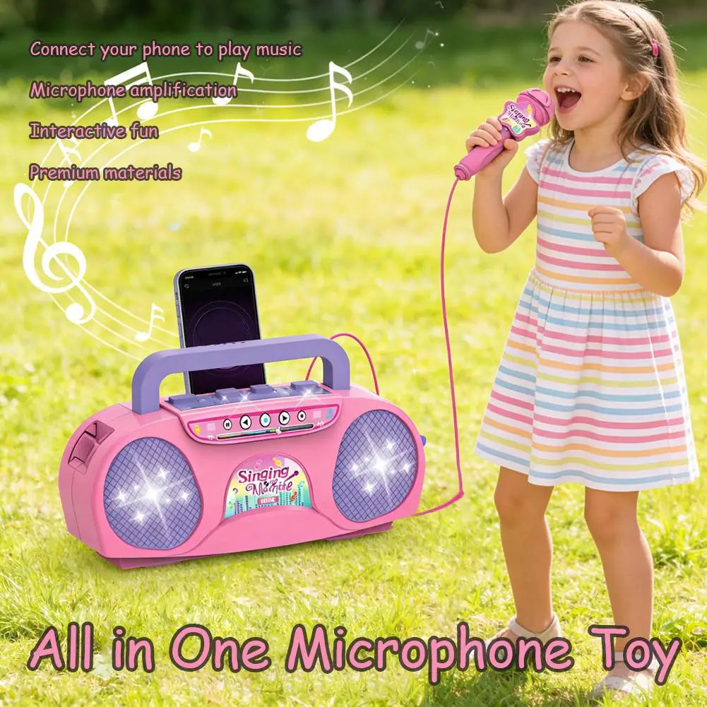 A young girl is singing into a pink microphone toy while a portable karaoke machine plays music nearby.