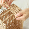 Hands weaving natural beige rattan strips into a storage basket