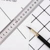 A black pen is placed next to a stainless steel precision ruler marked in millimeters on white paper.
