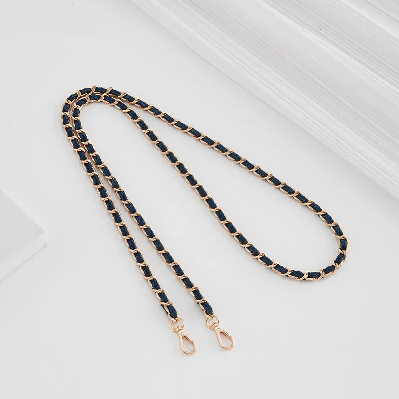 A close-up of a gold-toned metal shoulder strap buckle for a crossbody bag, featuring dark blue leather or fabric.