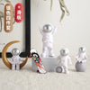 A set of handcrafted astronaut figurines in various colors and a wooden crescent moon on a desk