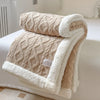 A beige double-layer fleece throw blanket folded on a white bed, showing the textured knit and fluffy trim.