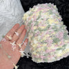 A hand holds a ball of hand-dyed variegated cotton blend yarn for knitting and crochet in pastel pink, green, and cream color