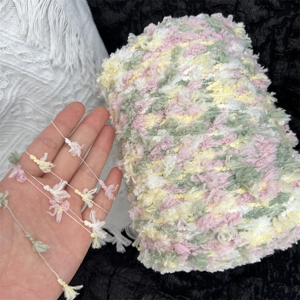 A hand holds a ball of hand-dyed variegated cotton blend yarn for knitting and crochet in pastel pink, green, and cream color