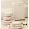 A set of white compressible packing cubes, including a large suitcase and several smaller bags, displayed on a light beige ca