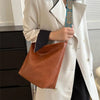 A woman holds a brown leather shoulder bag with blue and gold embroidery under a white blazer.