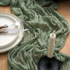 A crinkle gauze cheesecloth table runner draped over a wooden surface with cutlery and a white candle.