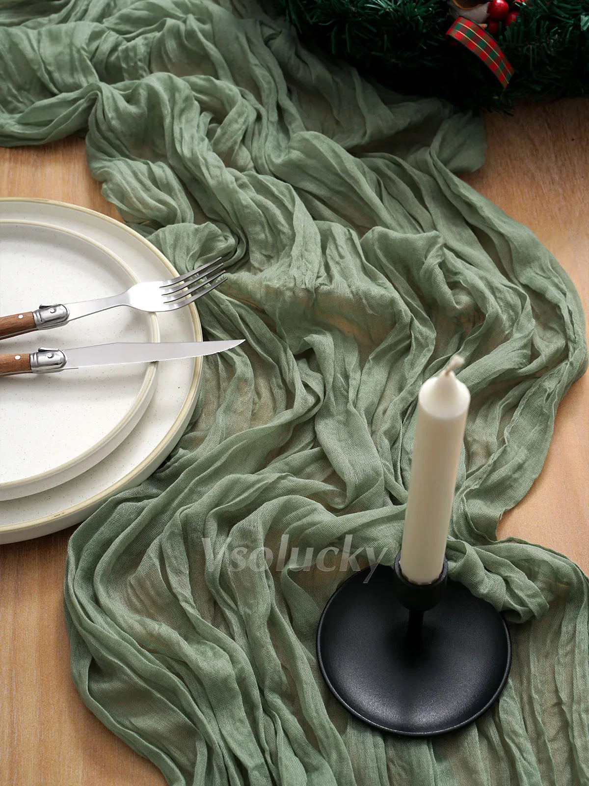 A crinkle gauze cheesecloth table runner draped over a wooden surface with cutlery and a white candle.