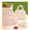 A pink quilted insulated lunch tote bag next to fresh fruit and a lemon on a white surface.