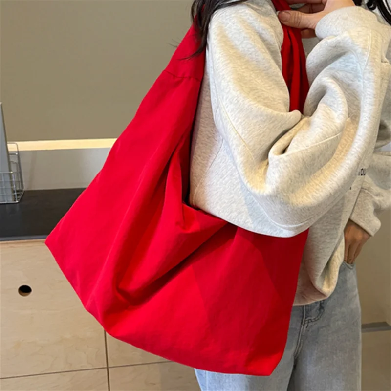 A person holds a bright red lightweight nylon tote bag against their chest.
