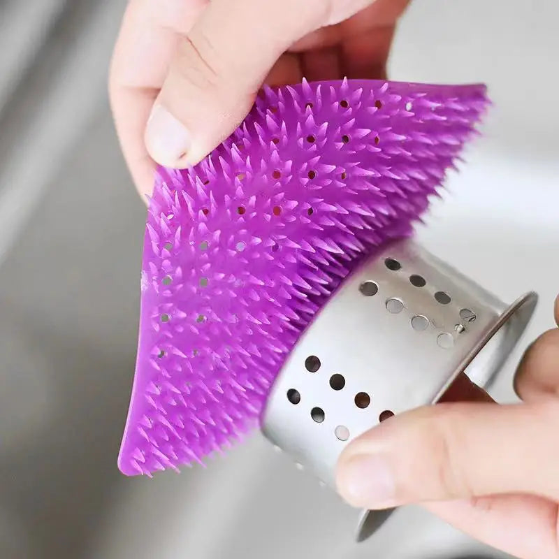 Une main tient un kit de gratte-éponge silicone violet et brosse à fissures contre un outil de nettoyage argenté.