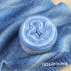 A roll of soft, blue and white gradient yarn is displayed on a blue fabric background.