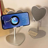 A silver heart-shaped stand holding a smartphone displaying a blue globe and a heart-shaped decorative stand.