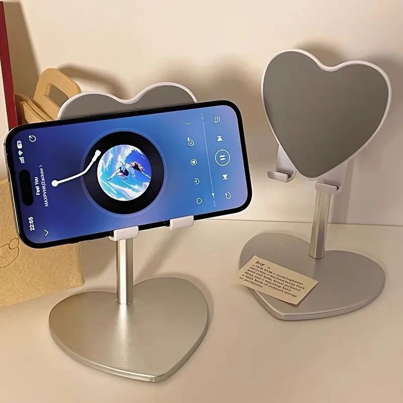A silver heart-shaped stand holding a smartphone displaying a blue globe and a heart-shaped decorative stand.