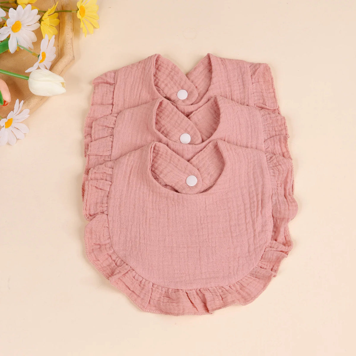 A set of three pink soft cotton ruffle bibs for babies displayed on a light background.