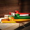 A golden kazoo rests on an open book with red and green objects in the background.