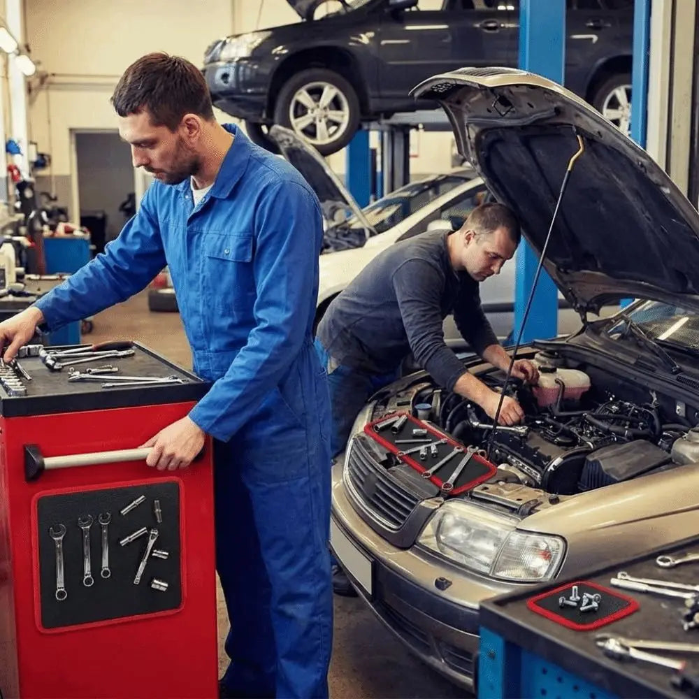 A mechanic in a blue jumpsuit works on a car engine with tools nearby.