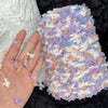 A hand holds a ball of hand-dyed variegated cotton blend yarn featuring purple, white, and peach tones.