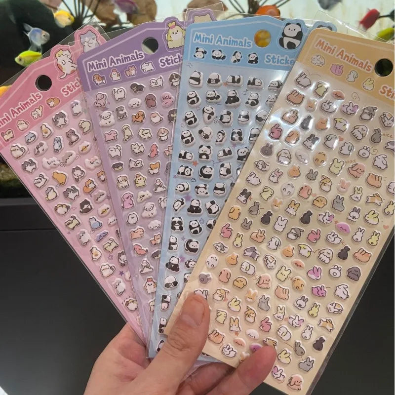 Eine Hand hält mehrere Blätter von Mini-Tieren-Dekosticker für das Journaling in verschiedenen Pastellfarben.