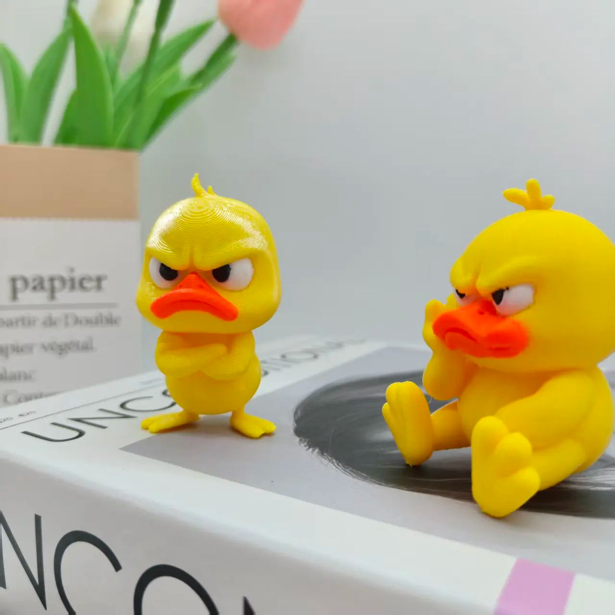 A yellow 3D printed duck statue decoration with an angry expression sitting on a white box.