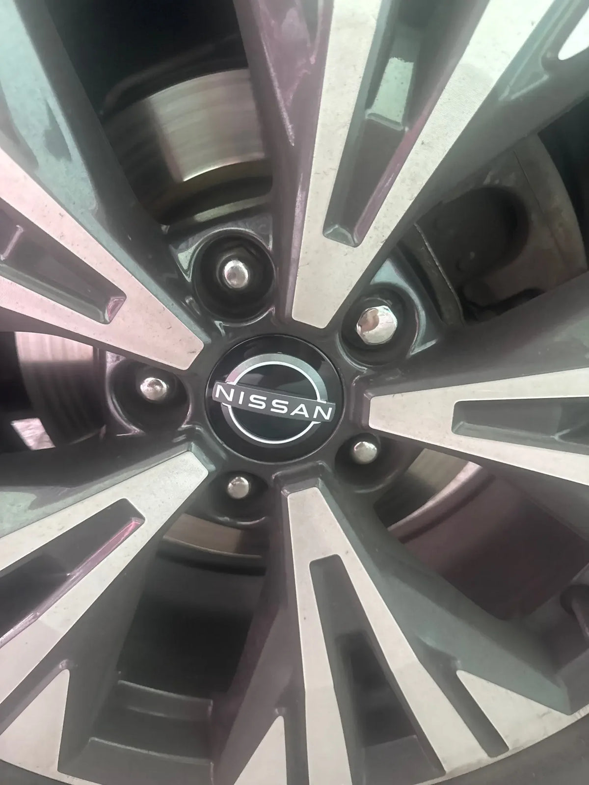 Close-up view of a Nissan wheel with four silver spoke hub caps.