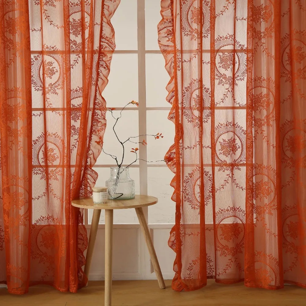 Orange sheer curtains with floral embroidery hanging in a window frame.