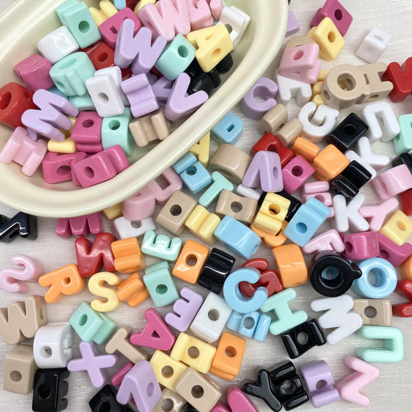 Une pile de perles de lettres acryliques colorées dans diverses nuances, incluant rose, violet, jaune et noir.