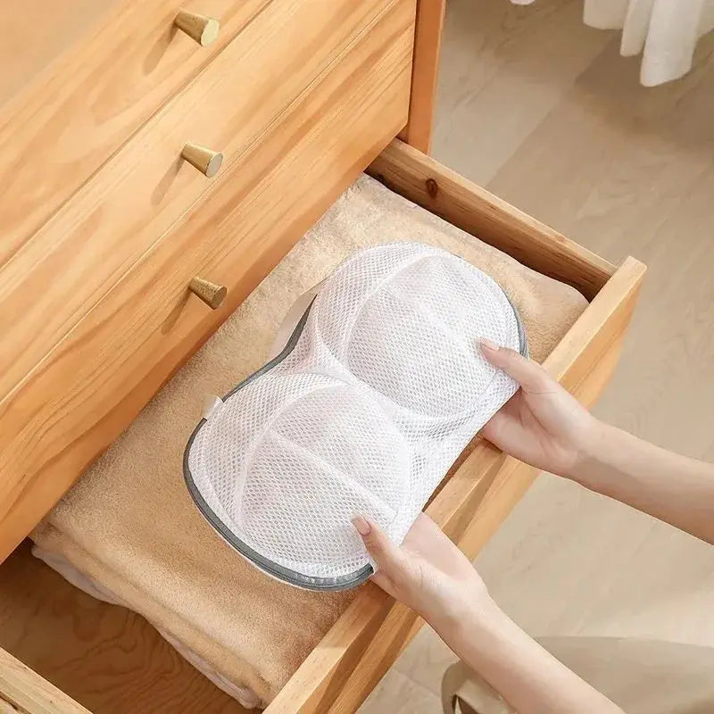A hand is holding a white fine mesh laundry bag for delicate underwear inside a wooden drawer.