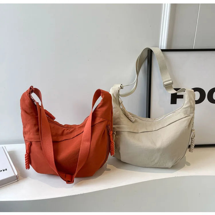 A light beige nylon crossbody bag with adjustable straps resting on a white surface.