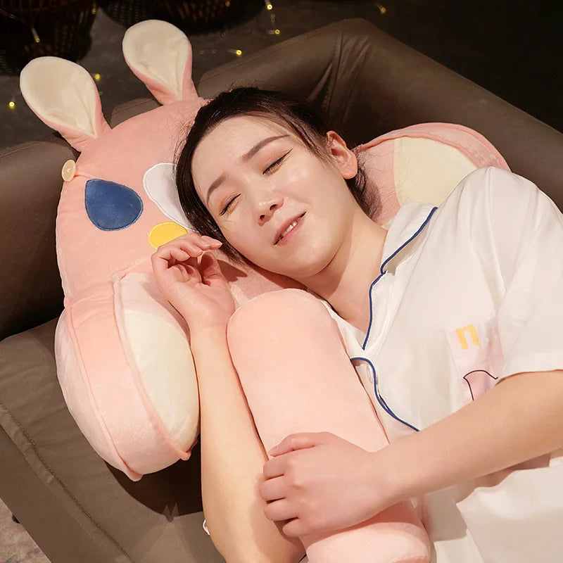 A person is resting their head on an adorable pink plush cat and dog backrest cushion while relaxing on a sofa.