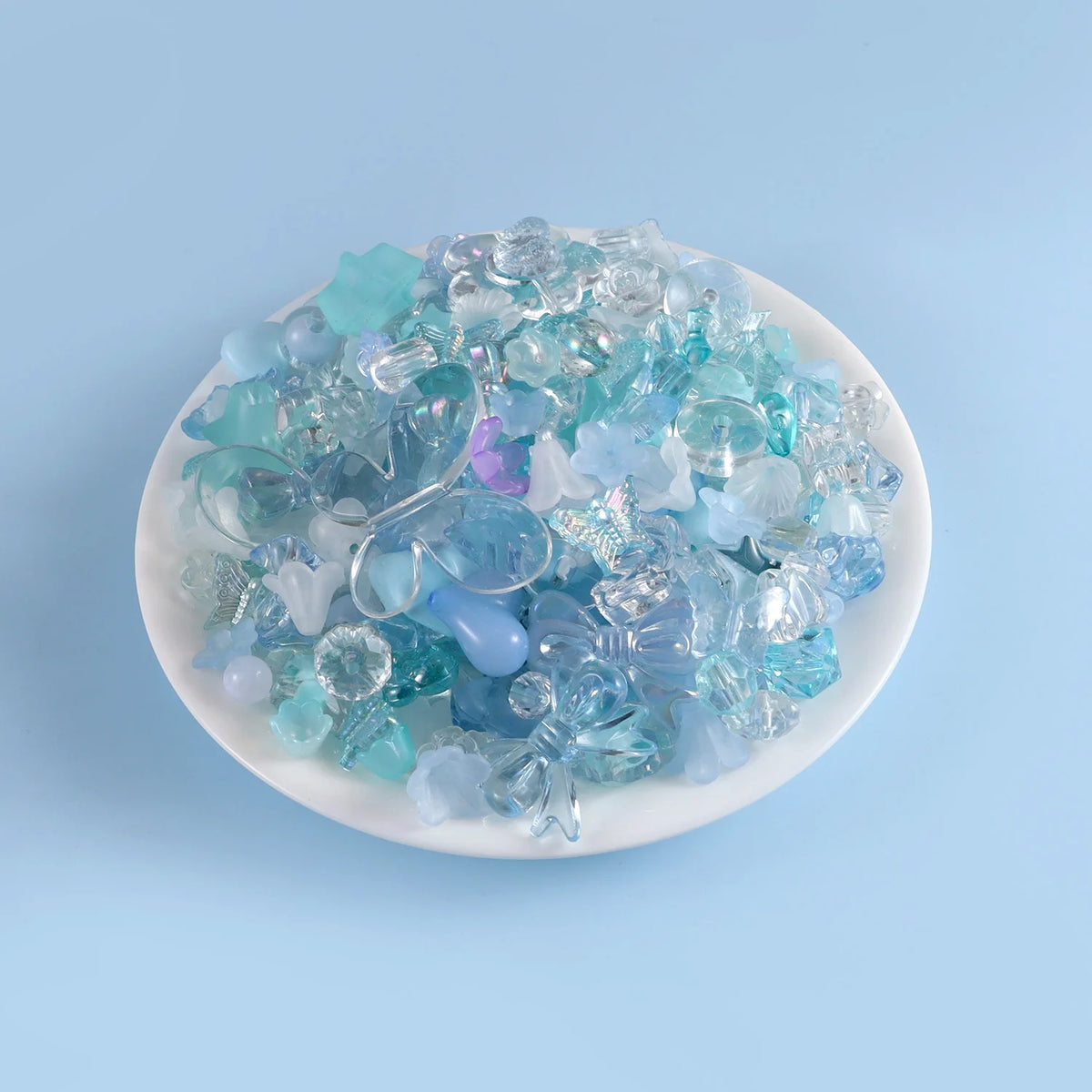 A pile of assorted blue and clear acrylic beads for DIY jewelry displayed on a white dish.