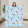 A woman holds up a light blue flannel throw blanket featuring cartoon designs of Masha and Bear.