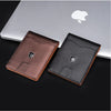 A dark brown and black carbon fiber wallet is displayed next to a silver laptop with an Apple logo.